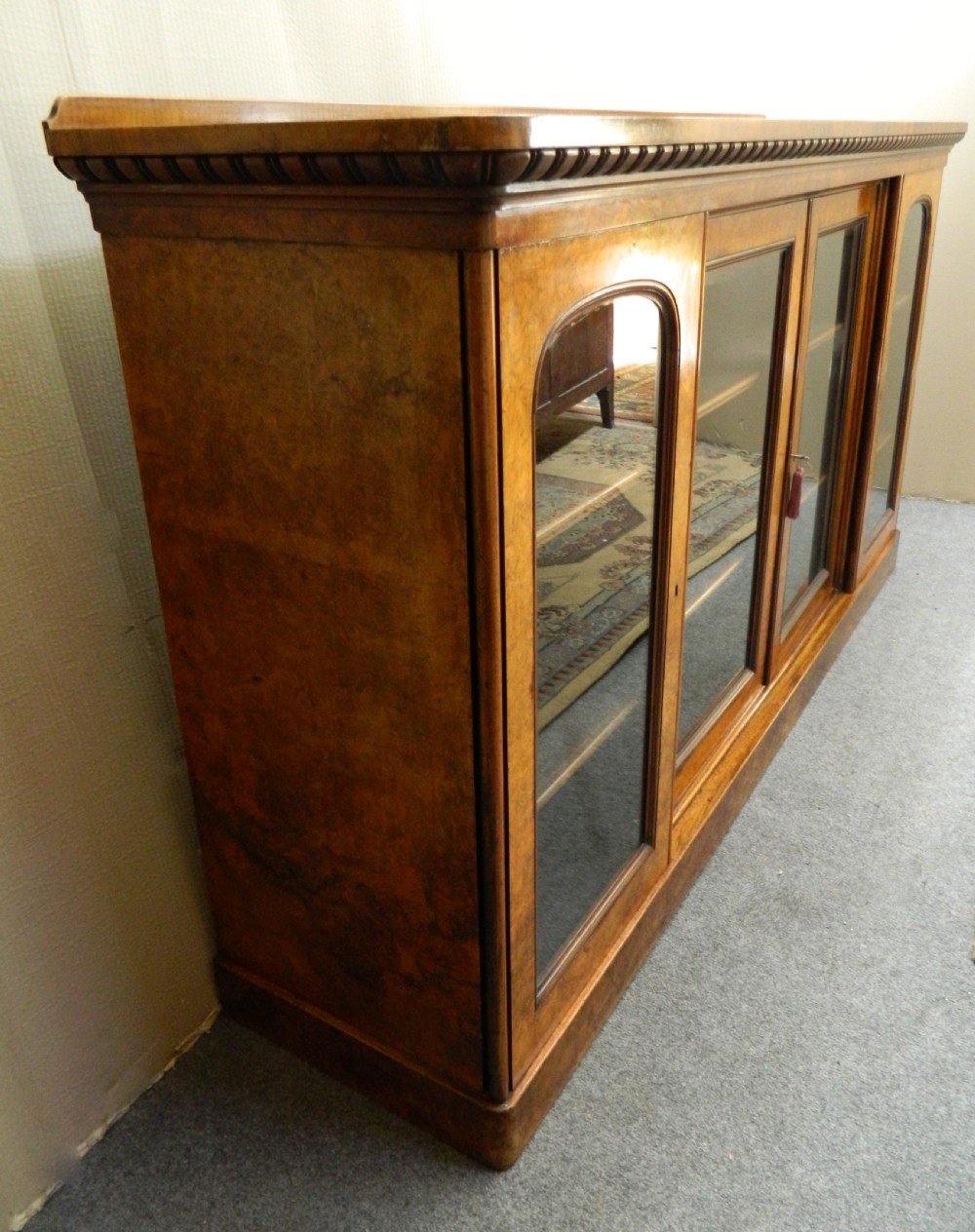 A large Victorian burr walnut bookcase featuring four glass-panelled doors, detailed wood grain patterning, and a solid plinth base. View V