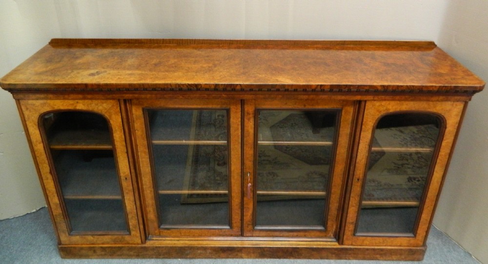 A large Victorian burr walnut bookcase featuring four glass-panelled doors, detailed wood grain patterning, and a solid plinth base. View VII