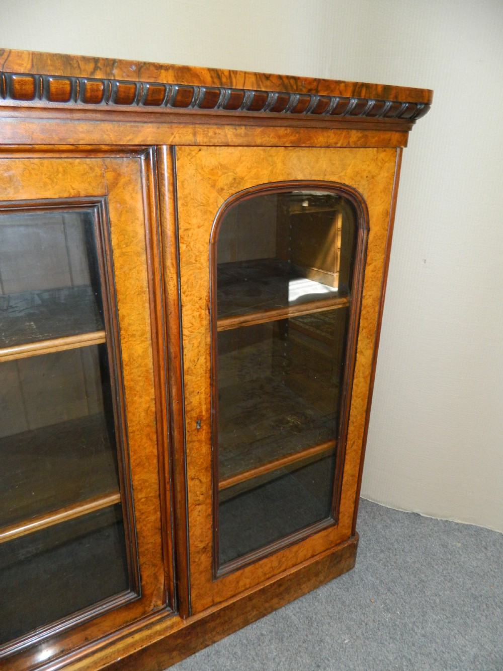 A large Victorian burr walnut bookcase featuring four glass-panelled doors, detailed wood grain patterning, and a solid plinth base. View IX