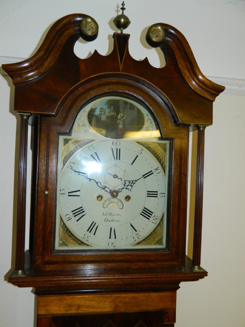 An antique Georgian mahogany longcase clock featuring a swan-neck pediment with brass finials, a painted arch dial, and string inlay details. View III