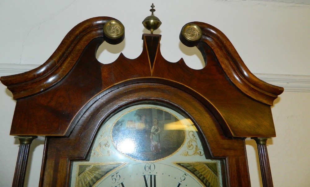 An antique Georgian mahogany longcase clock featuring a swan-neck pediment with brass finials, a painted arch dial, and string inlay details. View V