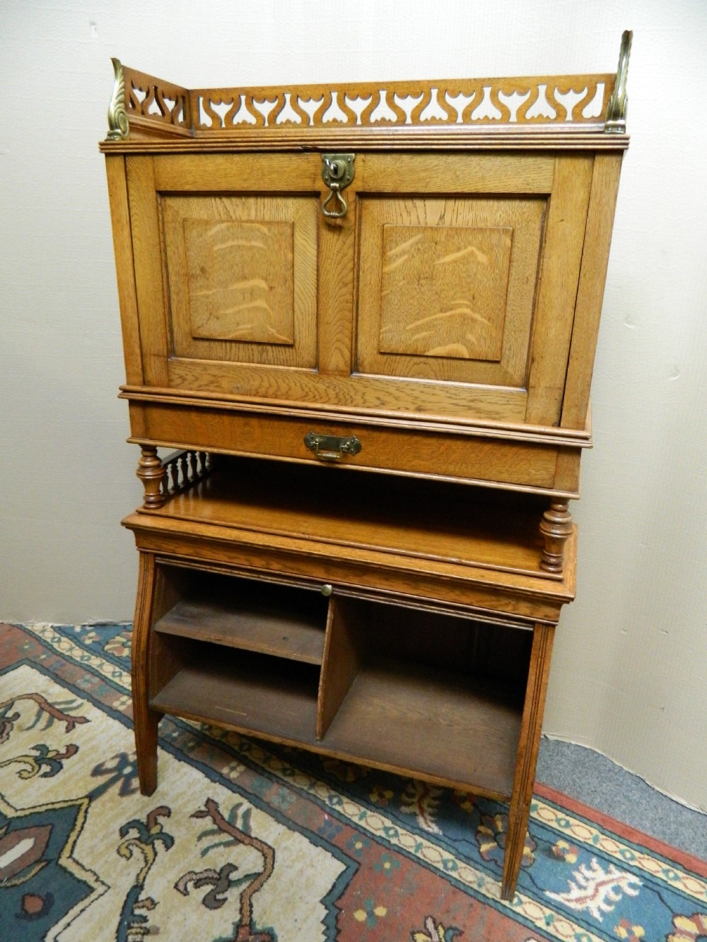 An Arts and Crafts golden oak bureau featuring a pierced heart gallery top, a fall-front writing section, a single drawer, an open spindle shelf, and a lower tambour front cabinet. View II