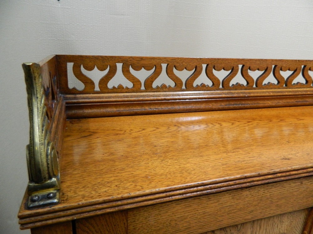 An Arts and Crafts golden oak bureau featuring a pierced heart gallery top, a fall-front writing section, a single drawer, an open spindle shelf, and a lower tambour front cabinet. View V