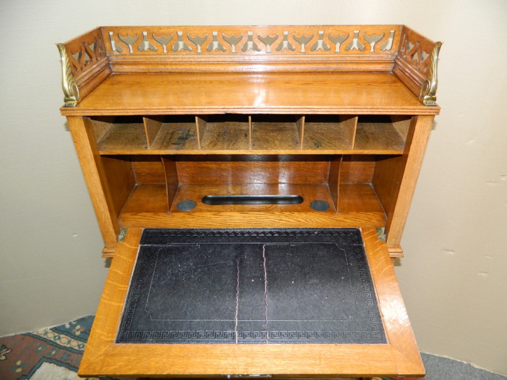 An Arts and Crafts golden oak bureau featuring a pierced heart gallery top, a fall-front writing section, a single drawer, an open spindle shelf, and a lower tambour front cabinet. View VI