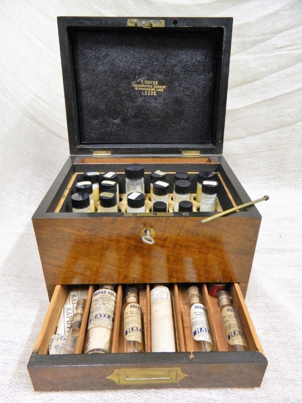 An opened Victorian mahogany apothecary chest displaying rows of glass medicine phials in fitted compartments and a lower drawer containing labelled bottles.