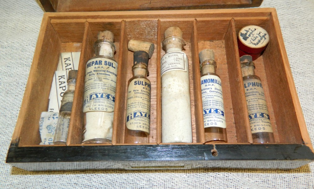 An opened Victorian mahogany apothecary chest displaying rows of glass medicine phials in fitted compartments and a lower drawer containing labelled bottles. View II