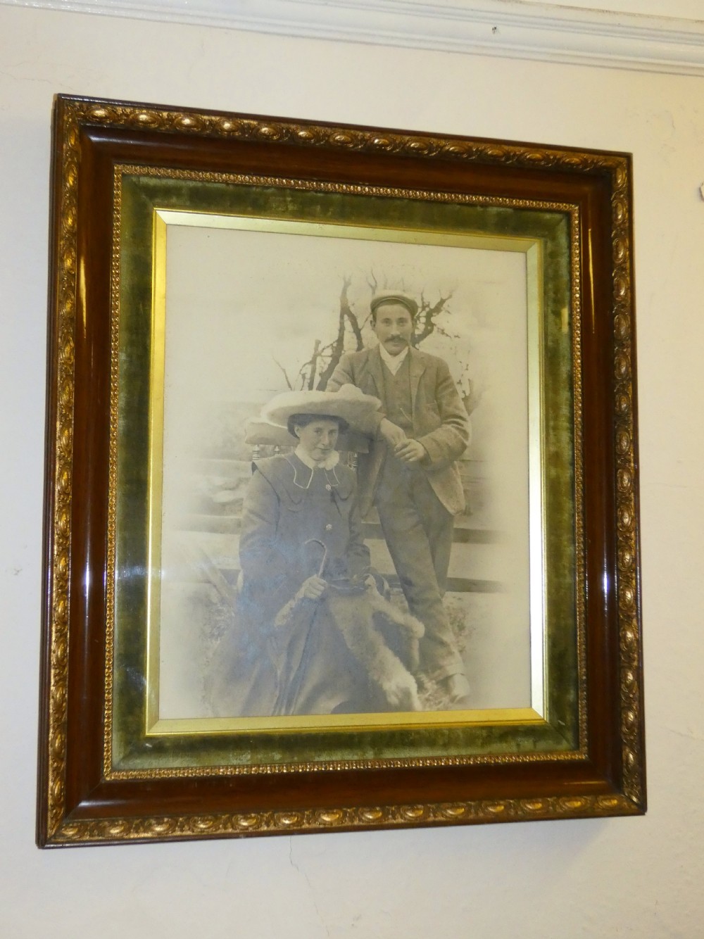 An antique monochrome portrait photograph of a man and woman displayed in a polished mahogany frame with a green velvet mount and decorative gilt slip.