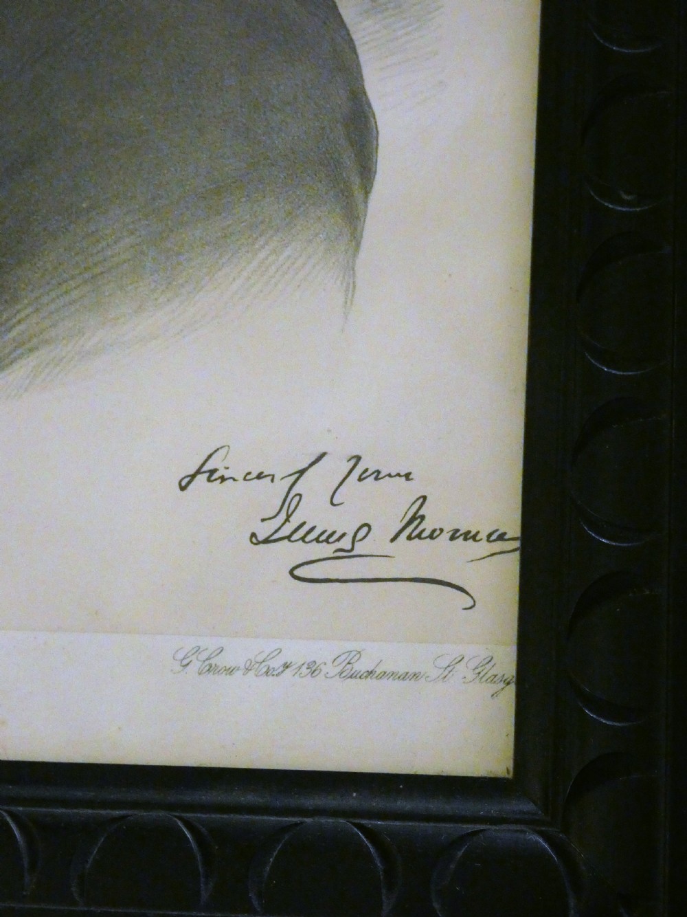 A monochrome antique framed portrait print depicting a Victorian gentleman wearing a top hat, presented in a dark carved wooden frame. View III