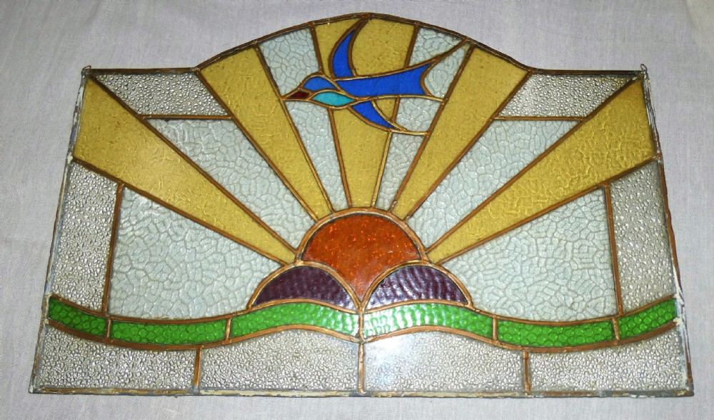 An Art Deco arched leaded stained glass panel depicting a blue bird flying above a sunburst motif over green hills. View II