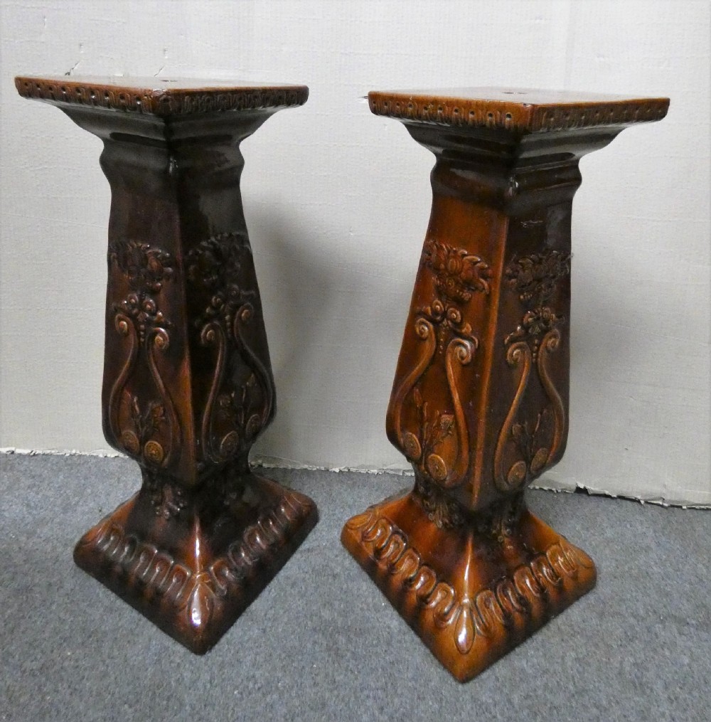 A pair of Arts and Crafts warm brown glazed earthenware plant stands featuring moulded relief scrollwork and square bases. View II