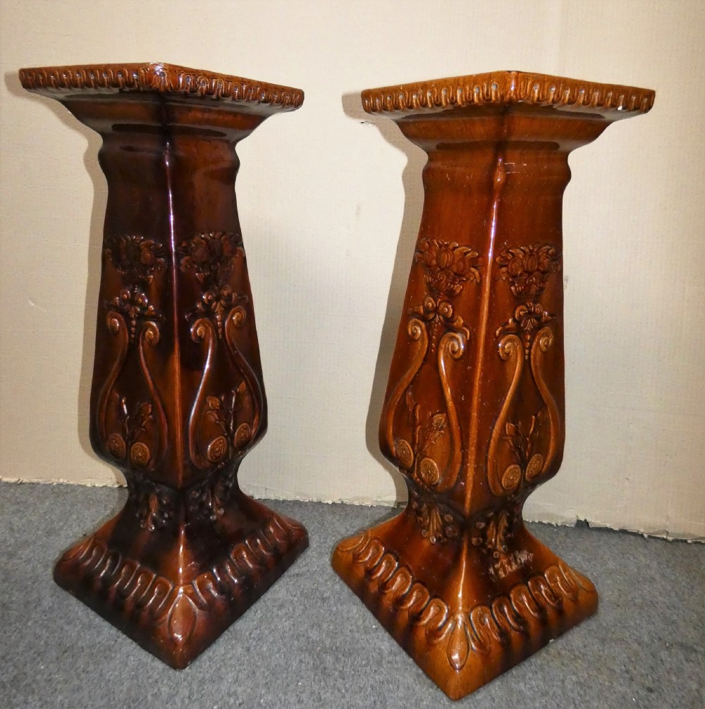 A pair of Arts and Crafts warm brown glazed earthenware plant stands featuring moulded relief scrollwork and square bases. View III