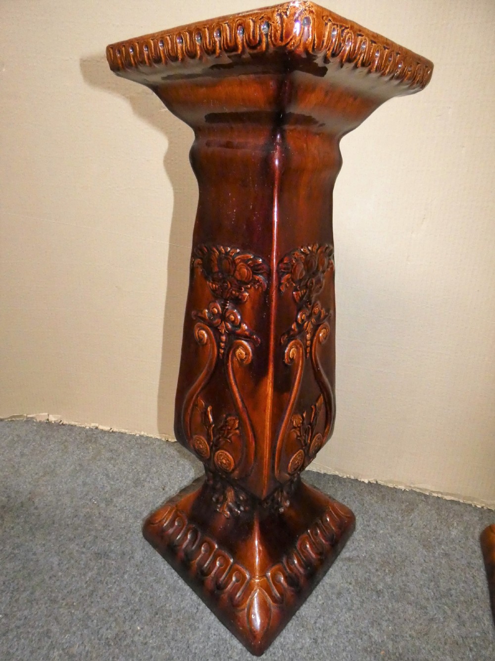 A pair of Arts and Crafts warm brown glazed earthenware plant stands featuring moulded relief scrollwork and square bases. View V