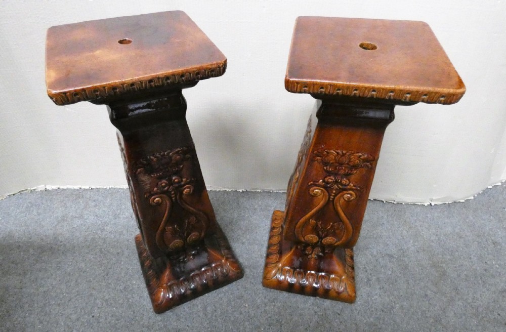 A pair of Arts and Crafts warm brown glazed earthenware plant stands featuring moulded relief scrollwork and square bases. View VI