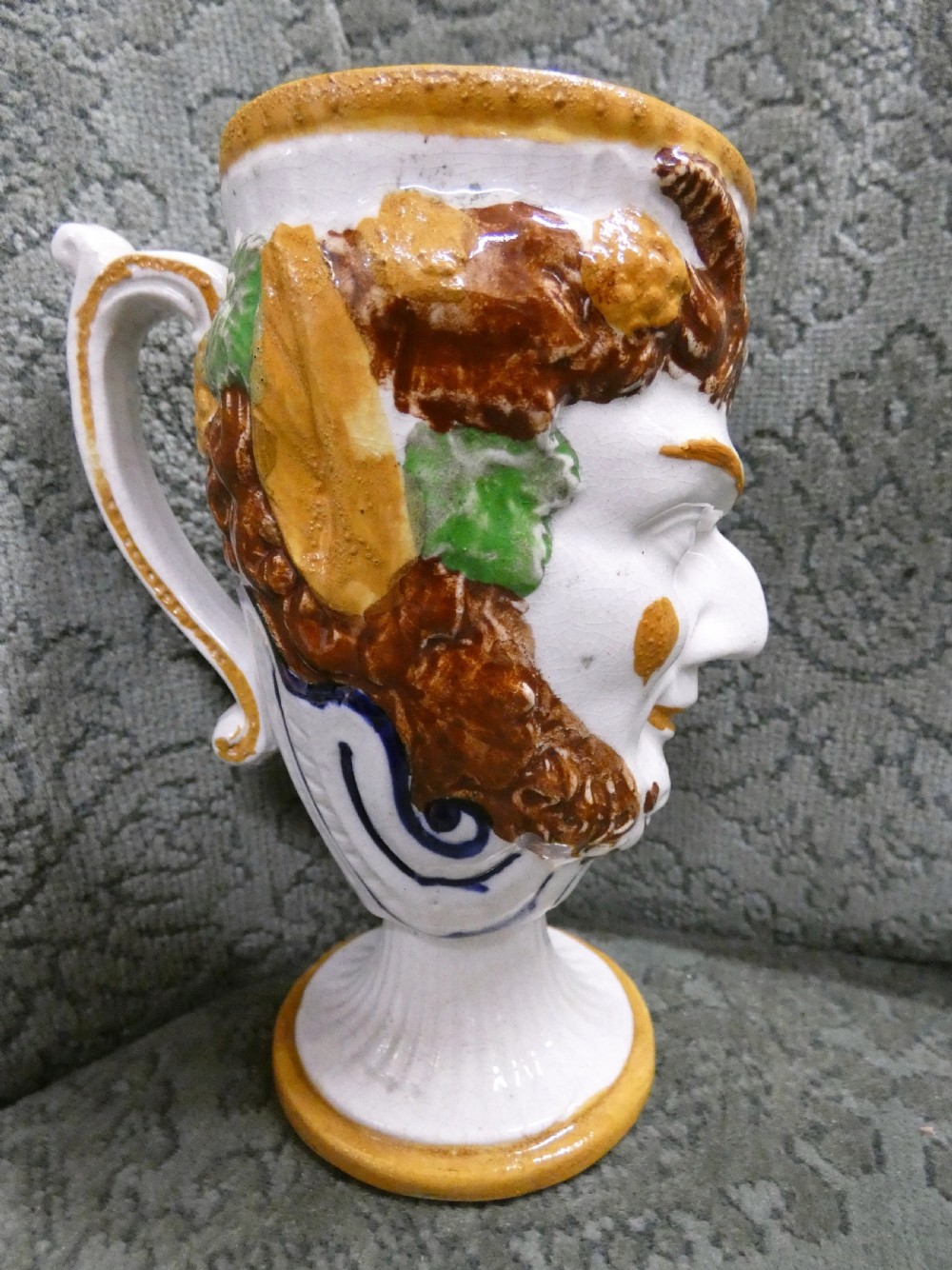 A Georgian Staffordshire earthenware mug moulded in the shape of the mythological figure Bacchus with polychrome glazes and a loop handle.