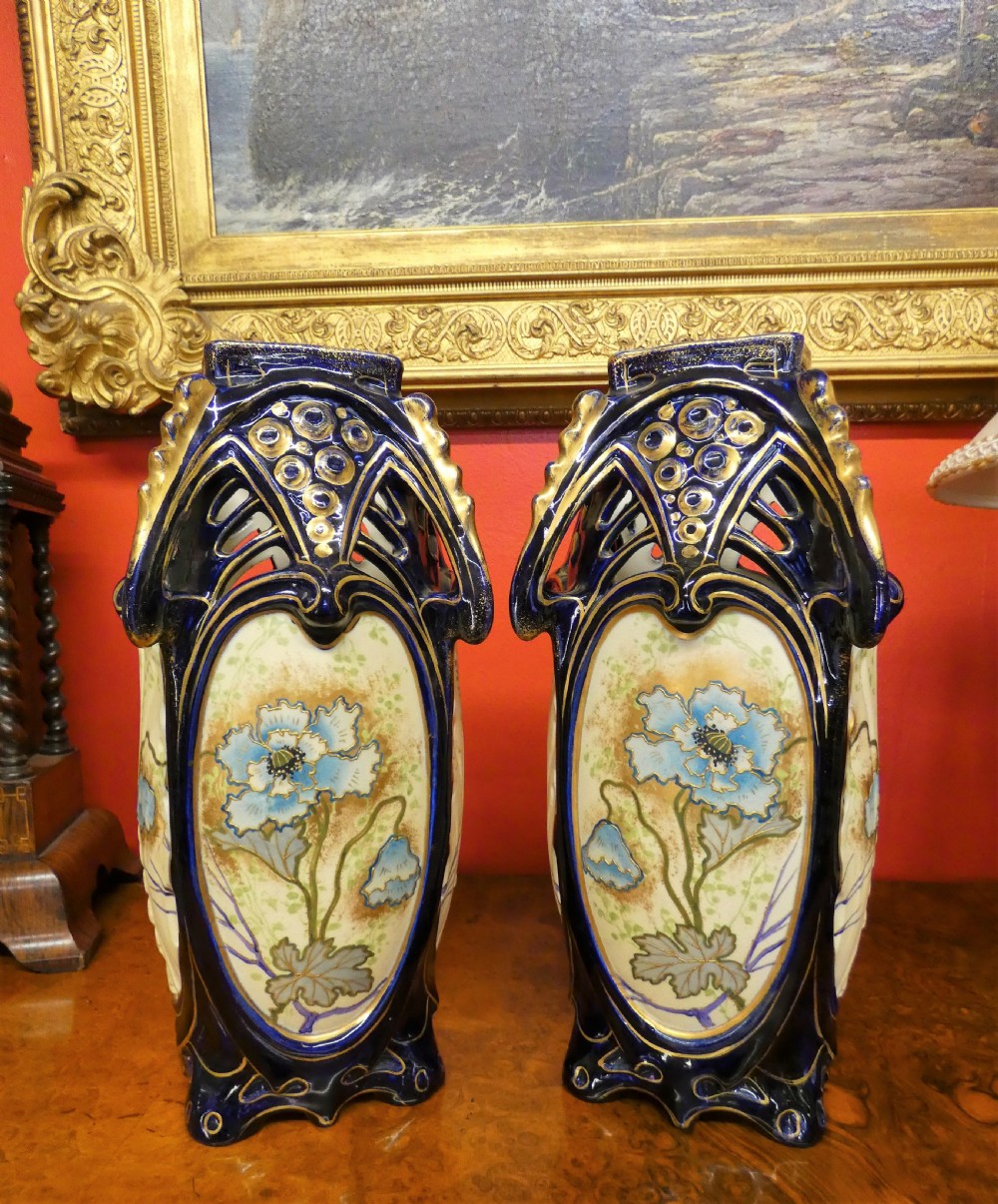 A pair of Art Nouveau ceramic vases with reticulated cobalt blue and gilt borders around hand-painted blue floral panels.