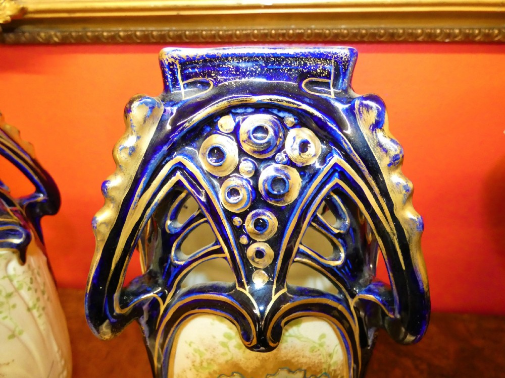 A pair of Art Nouveau ceramic vases with reticulated cobalt blue and gilt borders around hand-painted blue floral panels. View X
