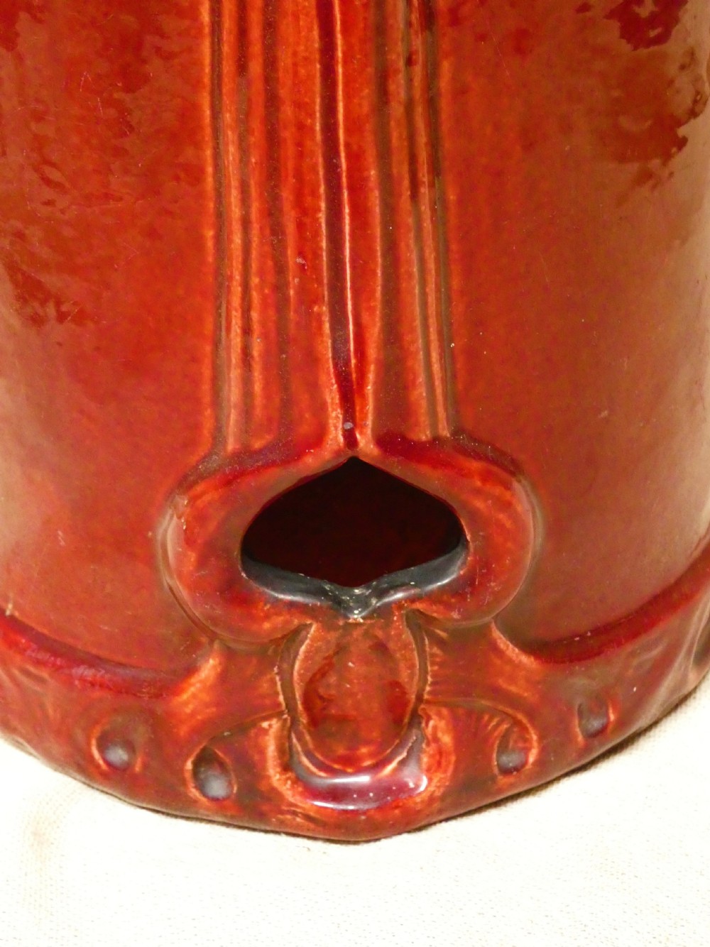 A tall cylindrical ceramic stick stand finished in a deep red glaze featuring an inset green relief panel with three thistle motifs. View IX