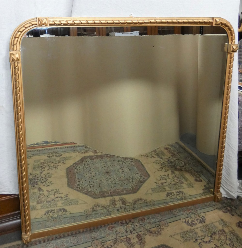 A large Victorian overmantel mirror featuring an arched gold giltwood frame with a rope-twist border and corner rosettes.