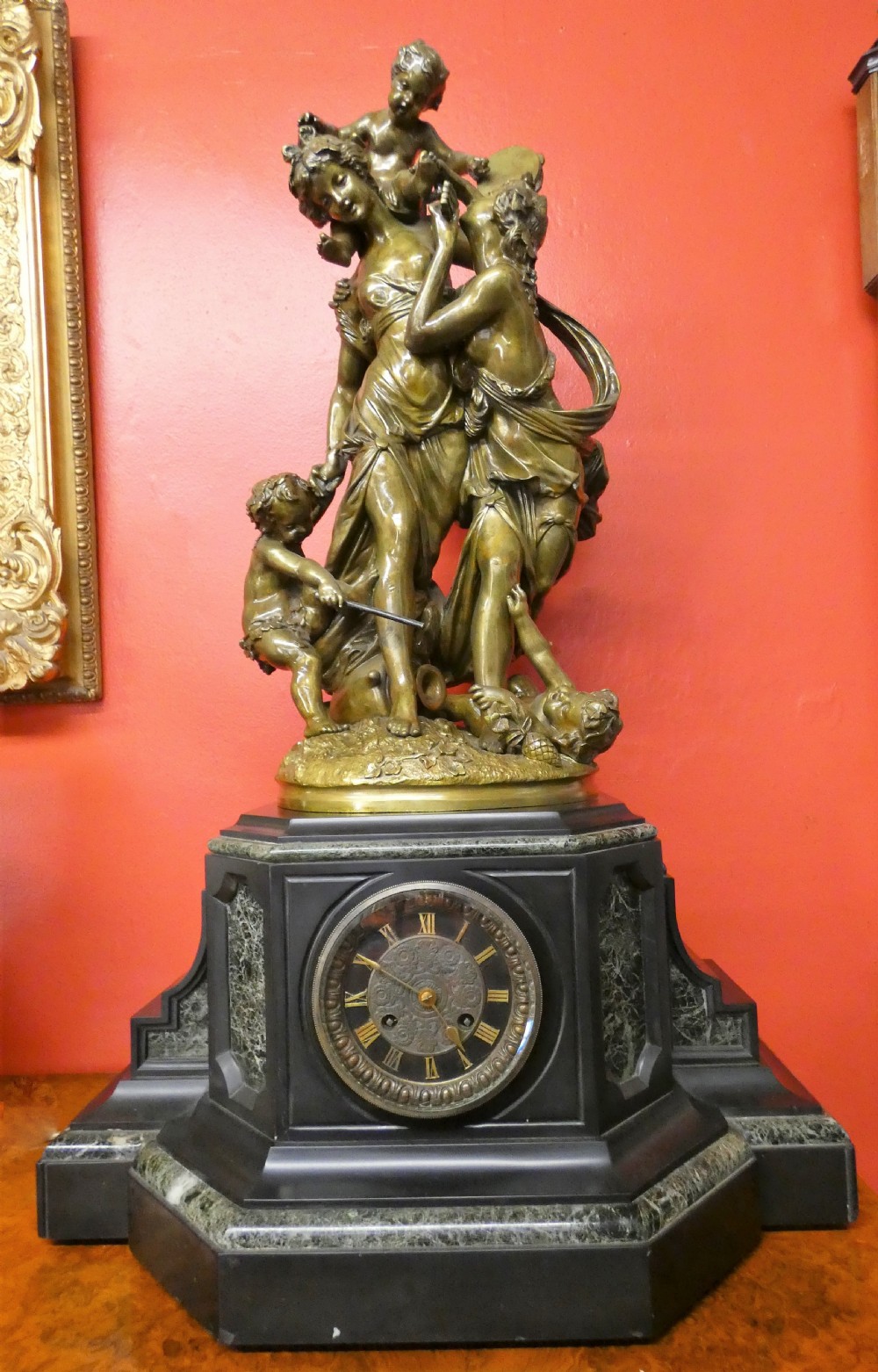 An antique French mantel clock featuring a dark marble base and a patinated bronze figural sculpture of classical figures on top.