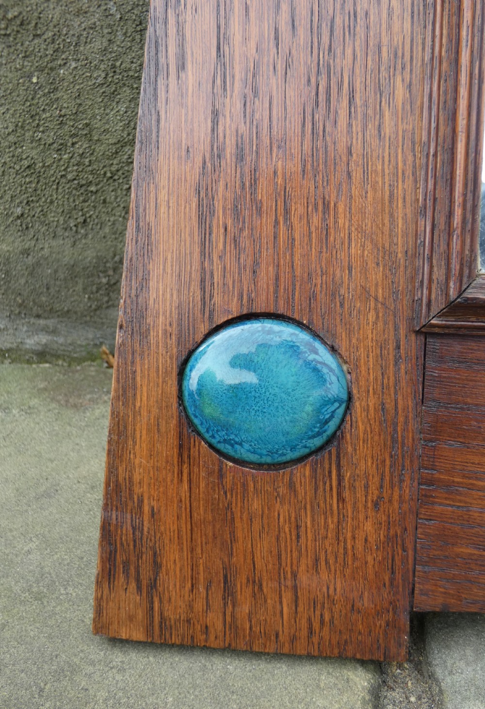 An Arts and Crafts style dark oak wall mirror featuring a carved arched crest and two round turquoise ceramic inlays in the lower corners. View III