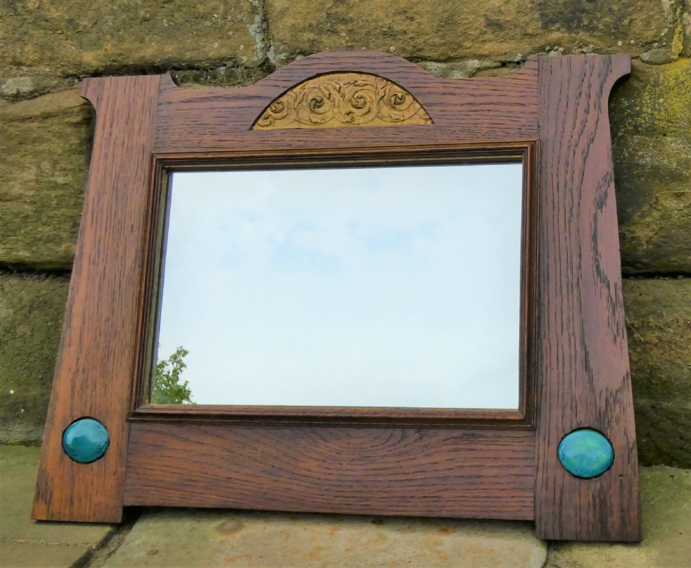 An Arts and Crafts style dark oak wall mirror featuring a carved arched crest and two round turquoise ceramic inlays in the lower corners. View IV