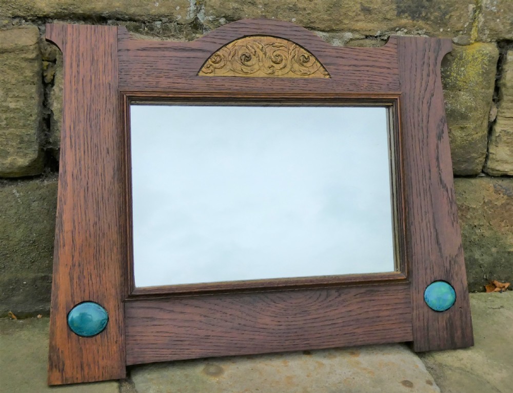 An Arts and Crafts style dark oak wall mirror featuring a carved arched crest and two round turquoise ceramic inlays in the lower corners. View V