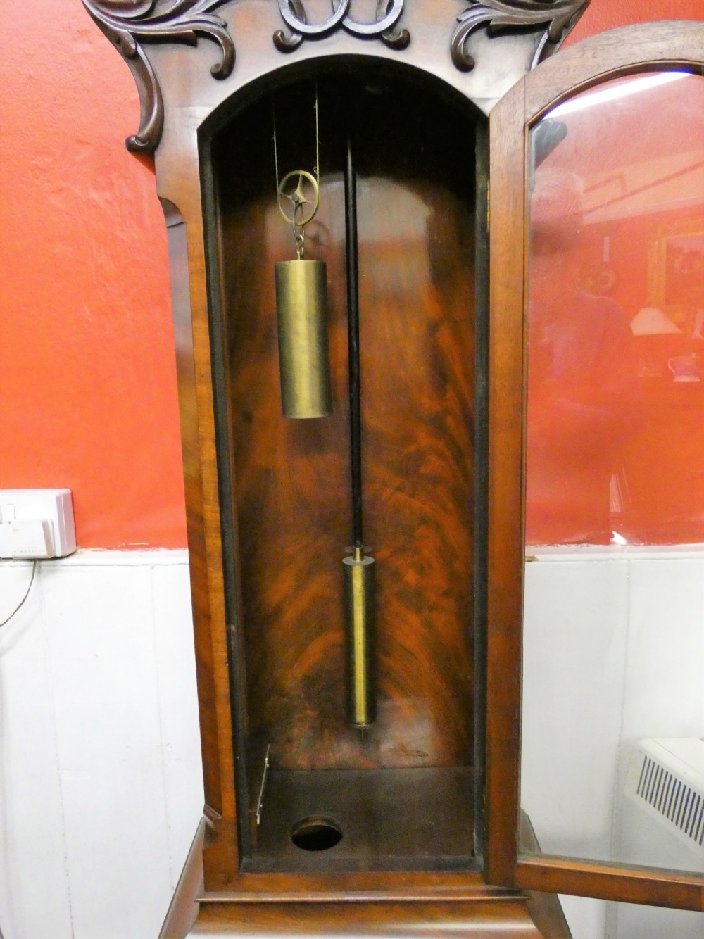 An antique carved dark mahogany regulator longcase clock featuring a circular dial, glass trunk door displaying pendulum weights, and a carved pedestal base. View VIII