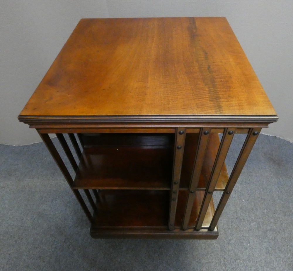 A dark polished mahogany revolving bookcase featuring vertical slatted sides with metal stud detail, multiple storage tiers, and a rotating base on castors. View V