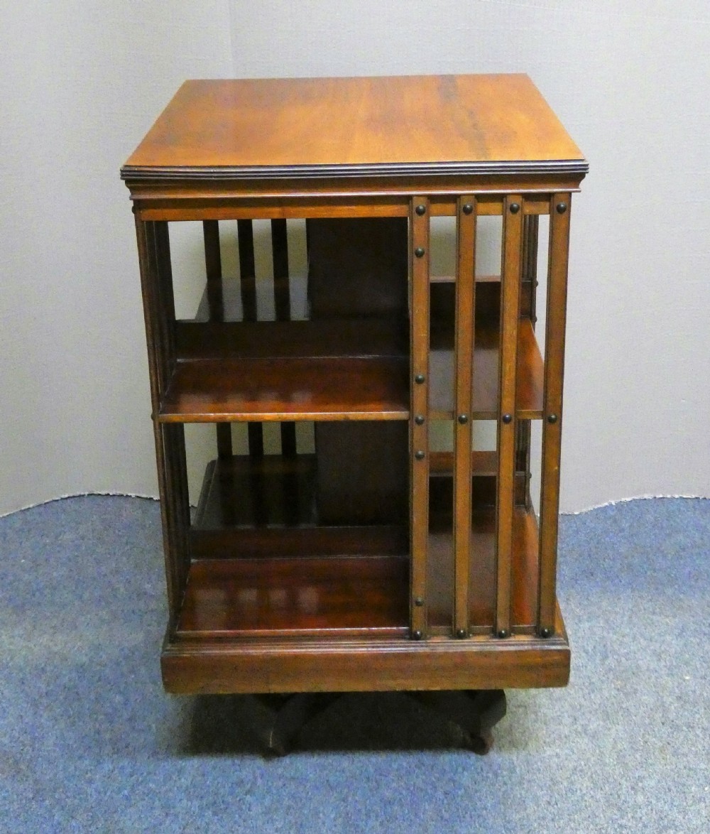 A dark polished mahogany revolving bookcase featuring vertical slatted sides with metal stud detail, multiple storage tiers, and a rotating base on castors. View VI