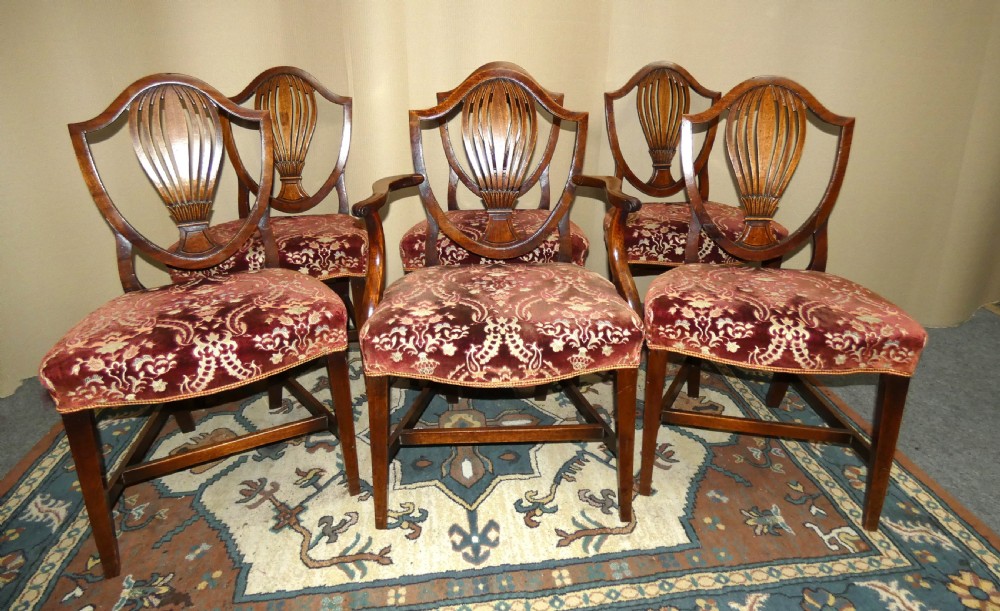 A set of six mahogany Hepplewhite dining chairs featuring carved shield backs and red patterned velvet upholstered seats.