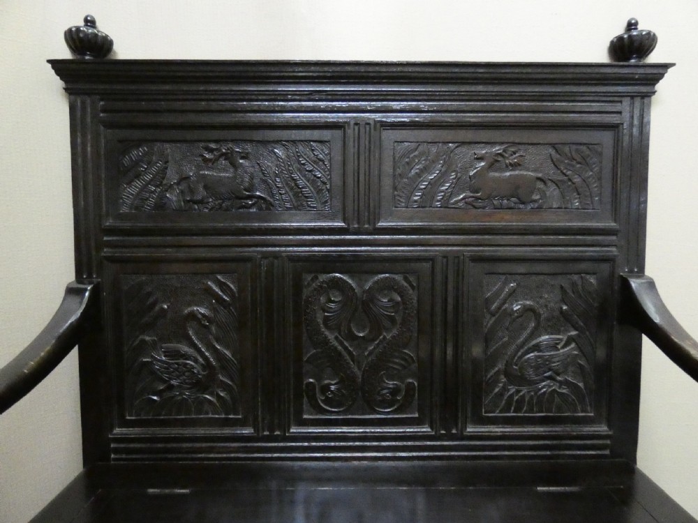 A dark carved oak high-back settle featuring relief panel carvings of swans and stags, turned arm supports, and a hinged box seat. View II