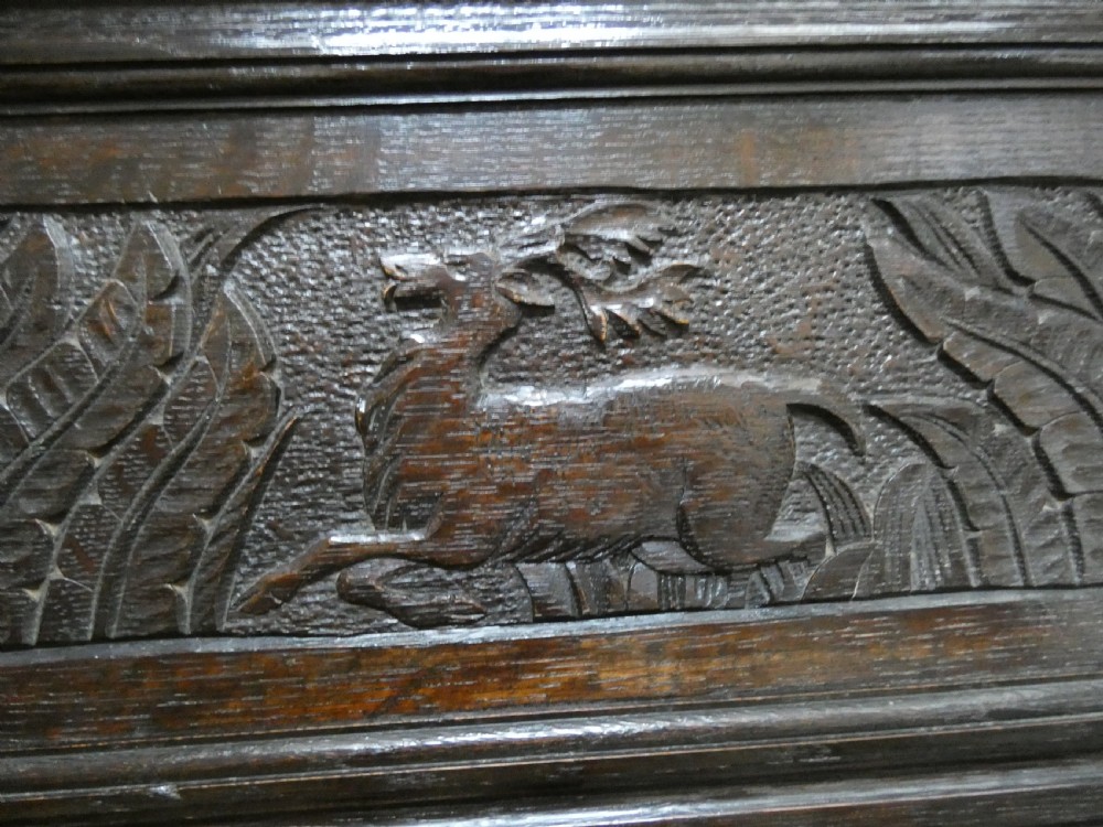 A dark carved oak high-back settle featuring relief panel carvings of swans and stags, turned arm supports, and a hinged box seat. View III