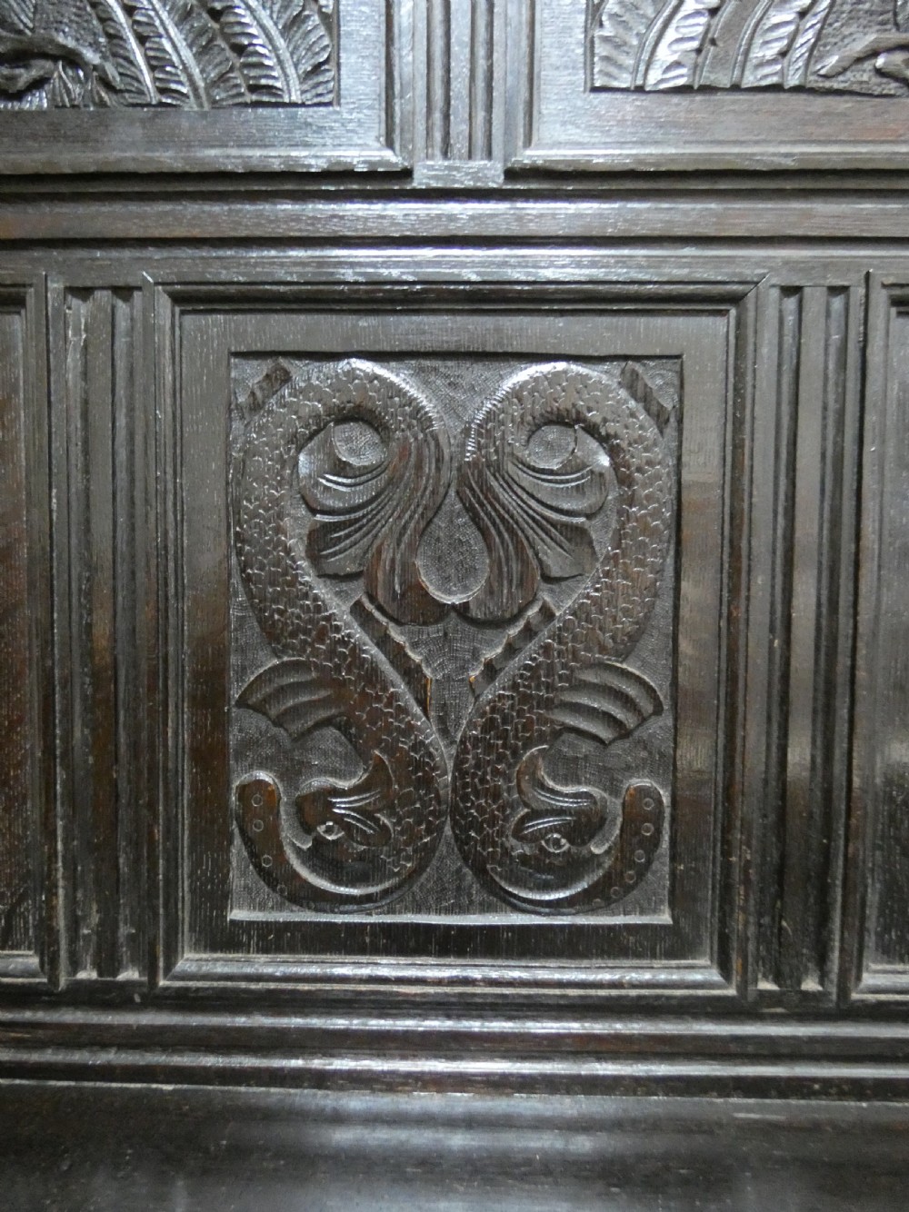 A dark carved oak high-back settle featuring relief panel carvings of swans and stags, turned arm supports, and a hinged box seat. View VI