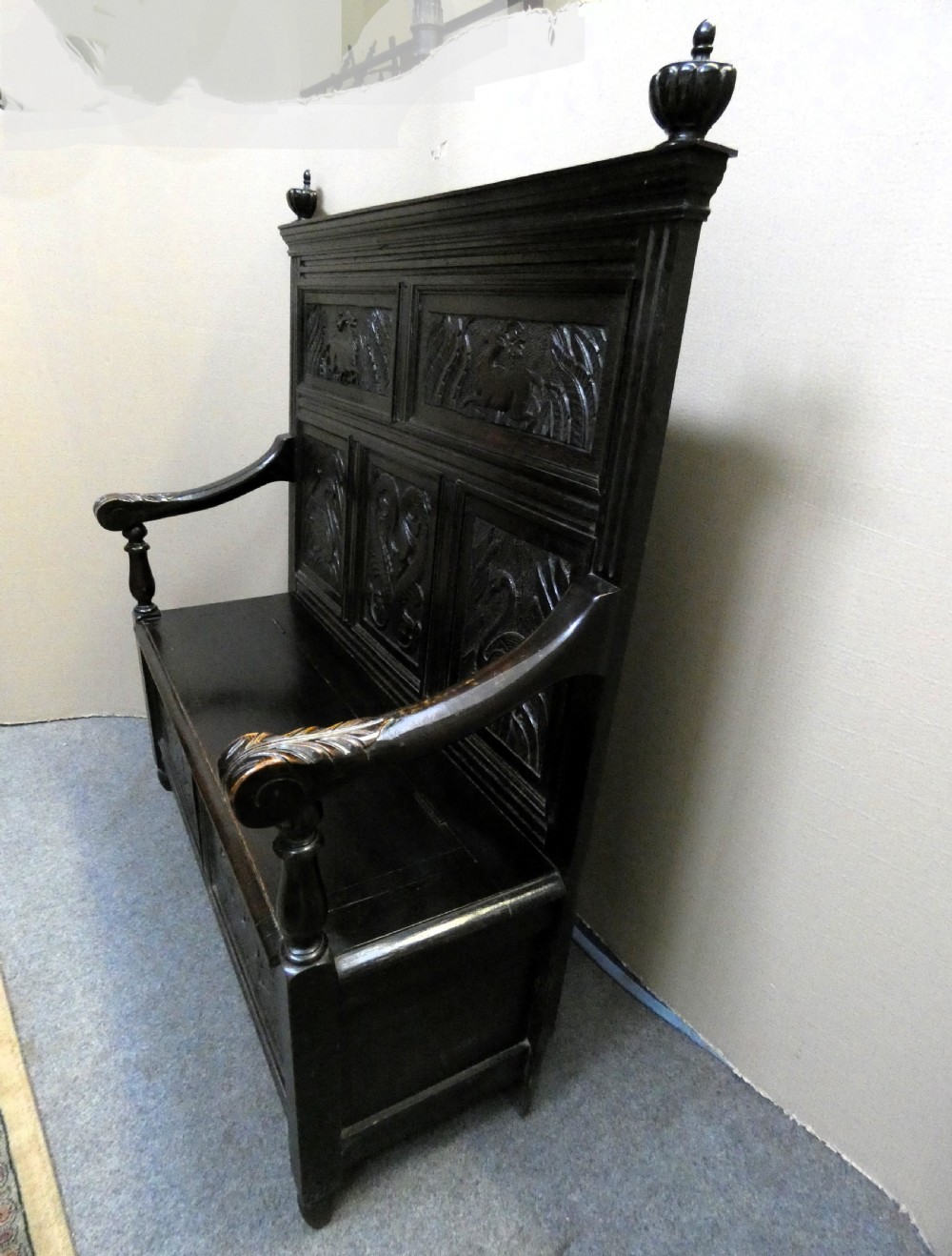 A dark carved oak high-back settle featuring relief panel carvings of swans and stags, turned arm supports, and a hinged box seat. View IX
