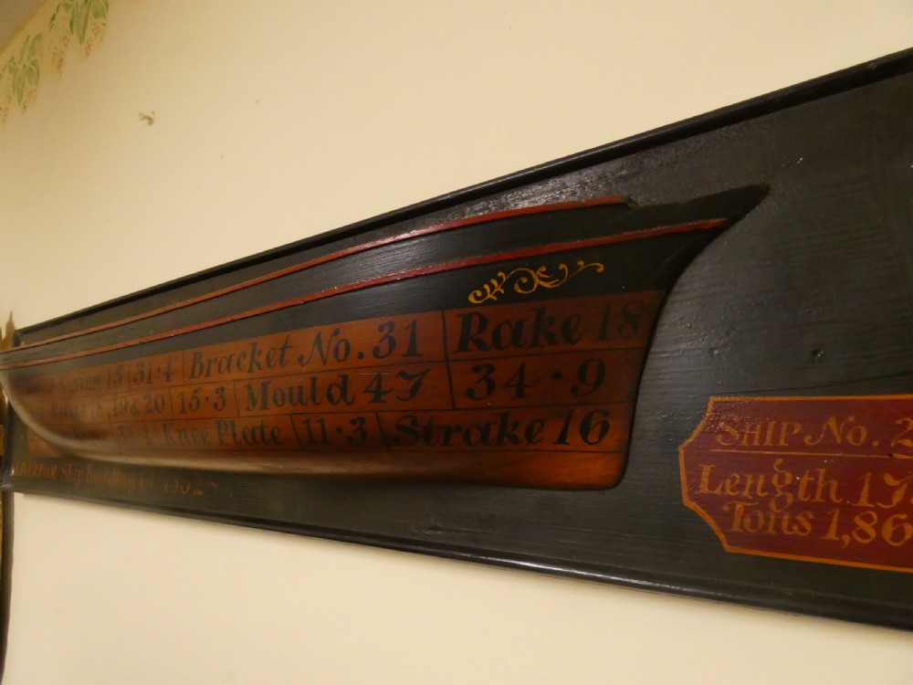A Victorian mounted half-hull ship model painted in terracotta and black with hand-written technical specifications on a black backboard. View III