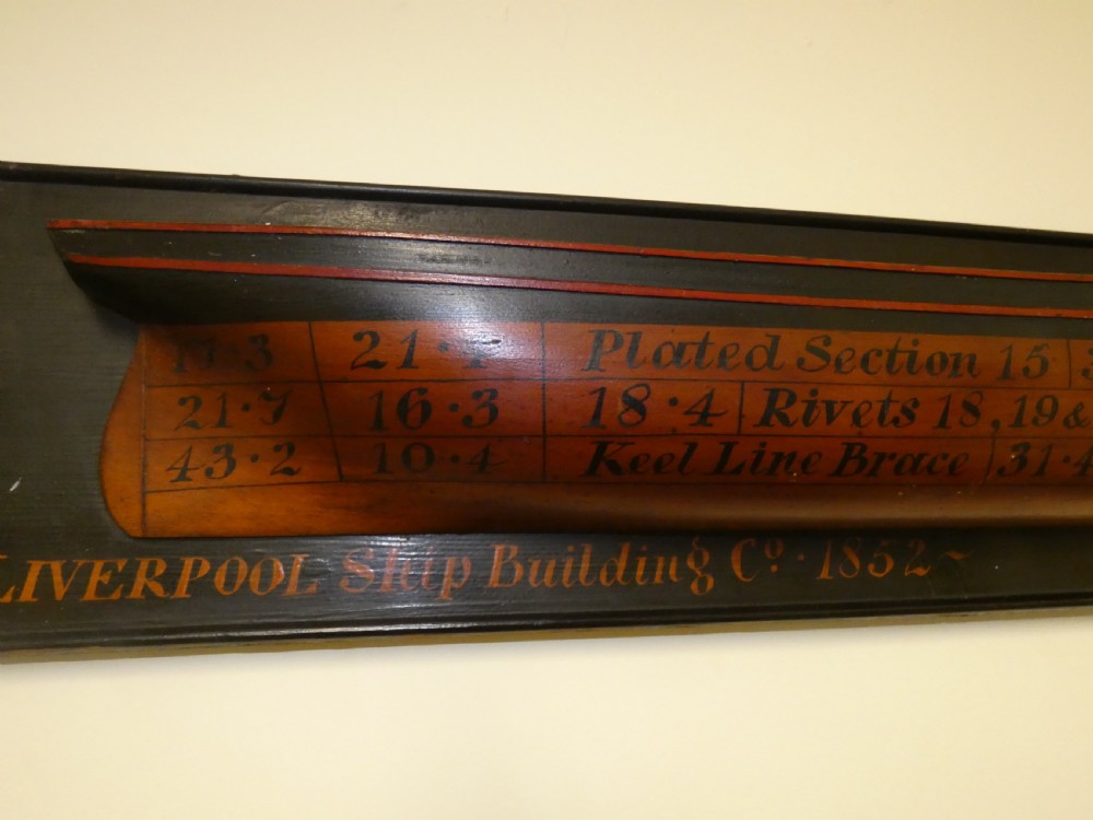 A Victorian mounted half-hull ship model painted in terracotta and black with hand-written technical specifications on a black backboard. View V