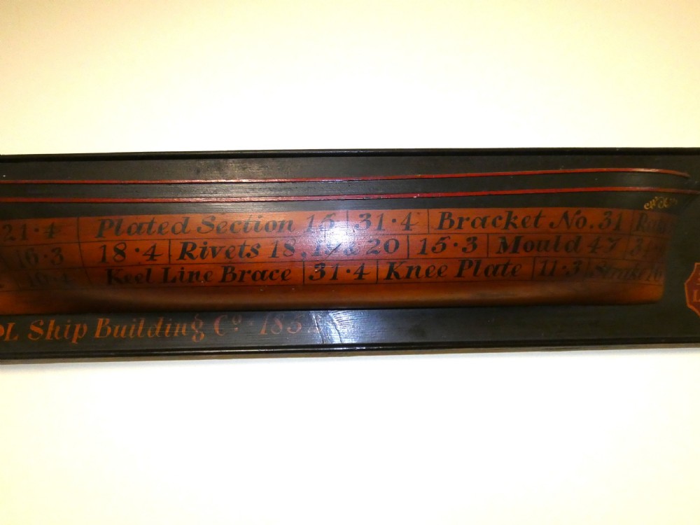 A Victorian mounted half-hull ship model painted in terracotta and black with hand-written technical specifications on a black backboard. View VI