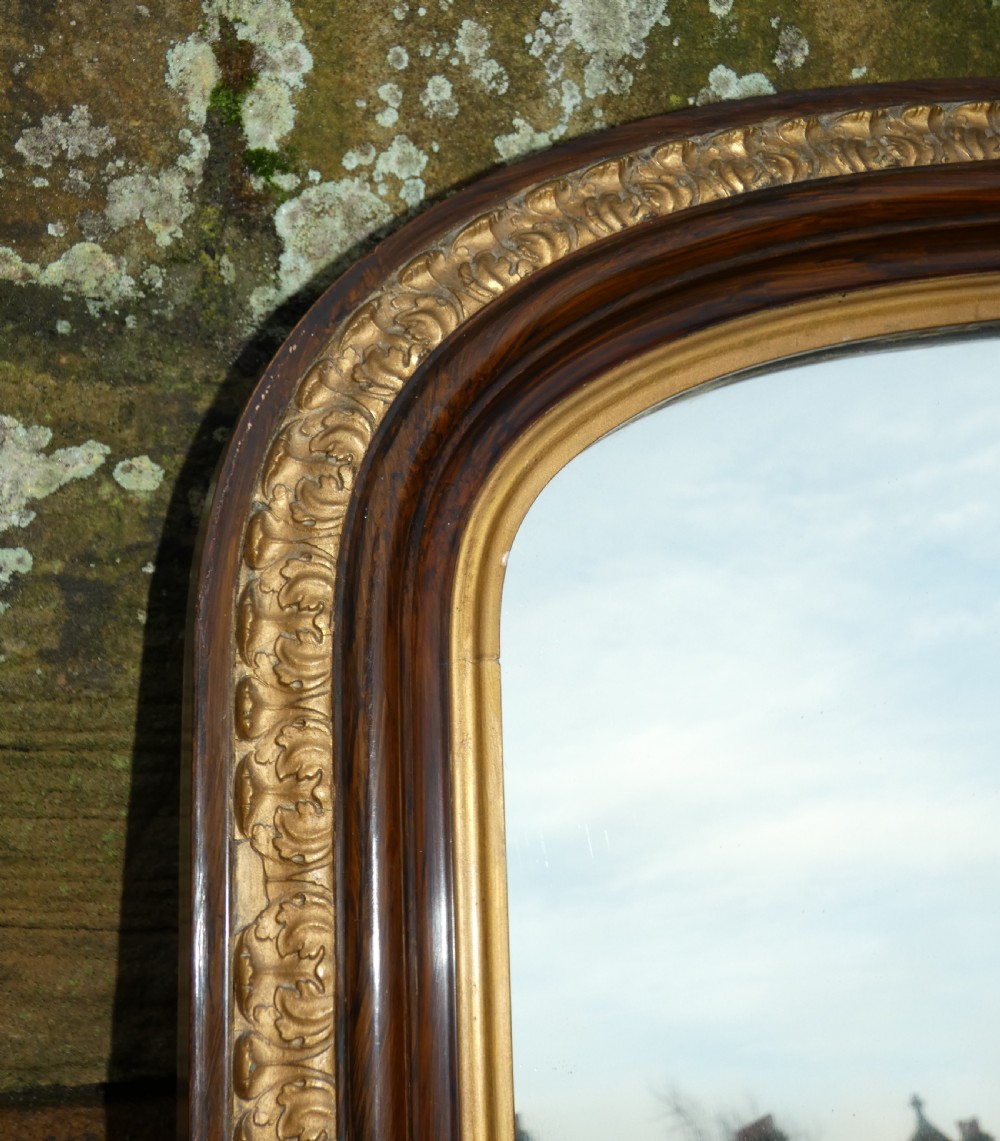 A Victorian arched overmantel mirror featuring a dark timber frame, inner gilt bead moulding, and white porcelain corner feet. View II