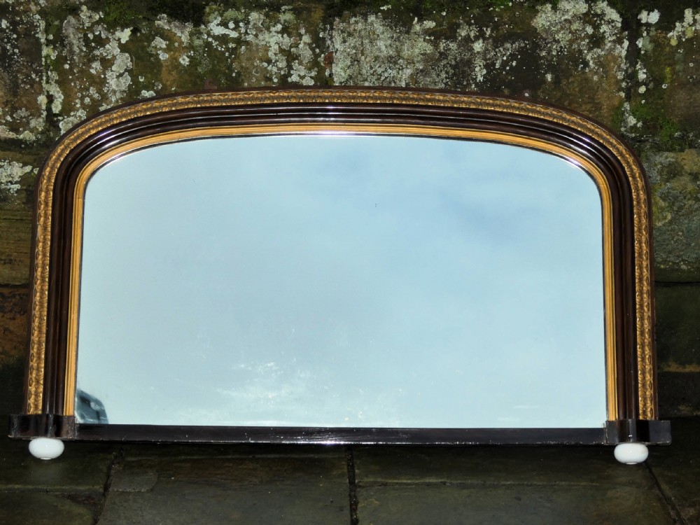 A Victorian arched overmantel mirror featuring a dark timber frame, inner gilt bead moulding, and white porcelain corner feet. View V