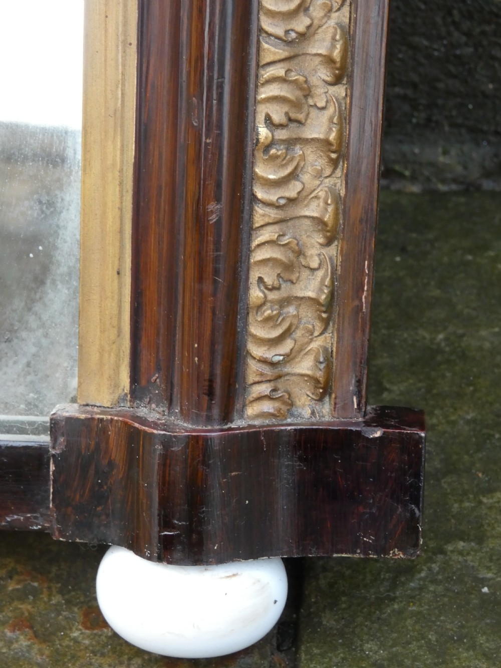 A Victorian arched overmantel mirror featuring a dark timber frame, inner gilt bead moulding, and white porcelain corner feet. View VI