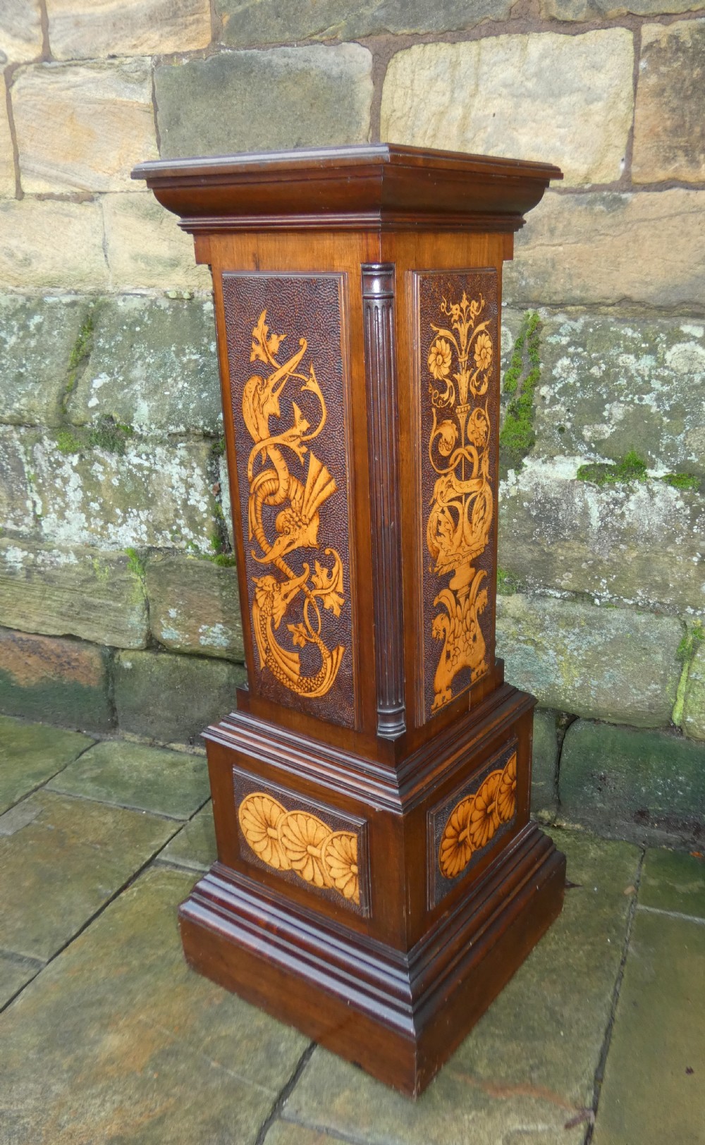 A square mahogany pedestal stand decorated with light-wood marquetry inlays featuring scrollwork and urn motifs on a stippled background.