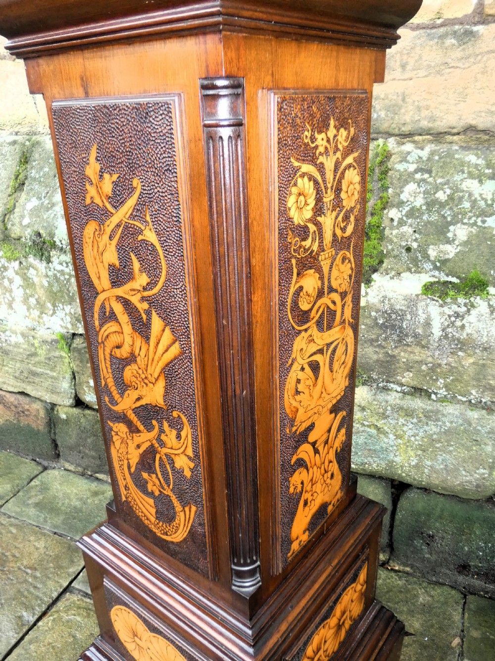 A square mahogany pedestal stand decorated with light-wood marquetry inlays featuring scrollwork and urn motifs on a stippled background. View II