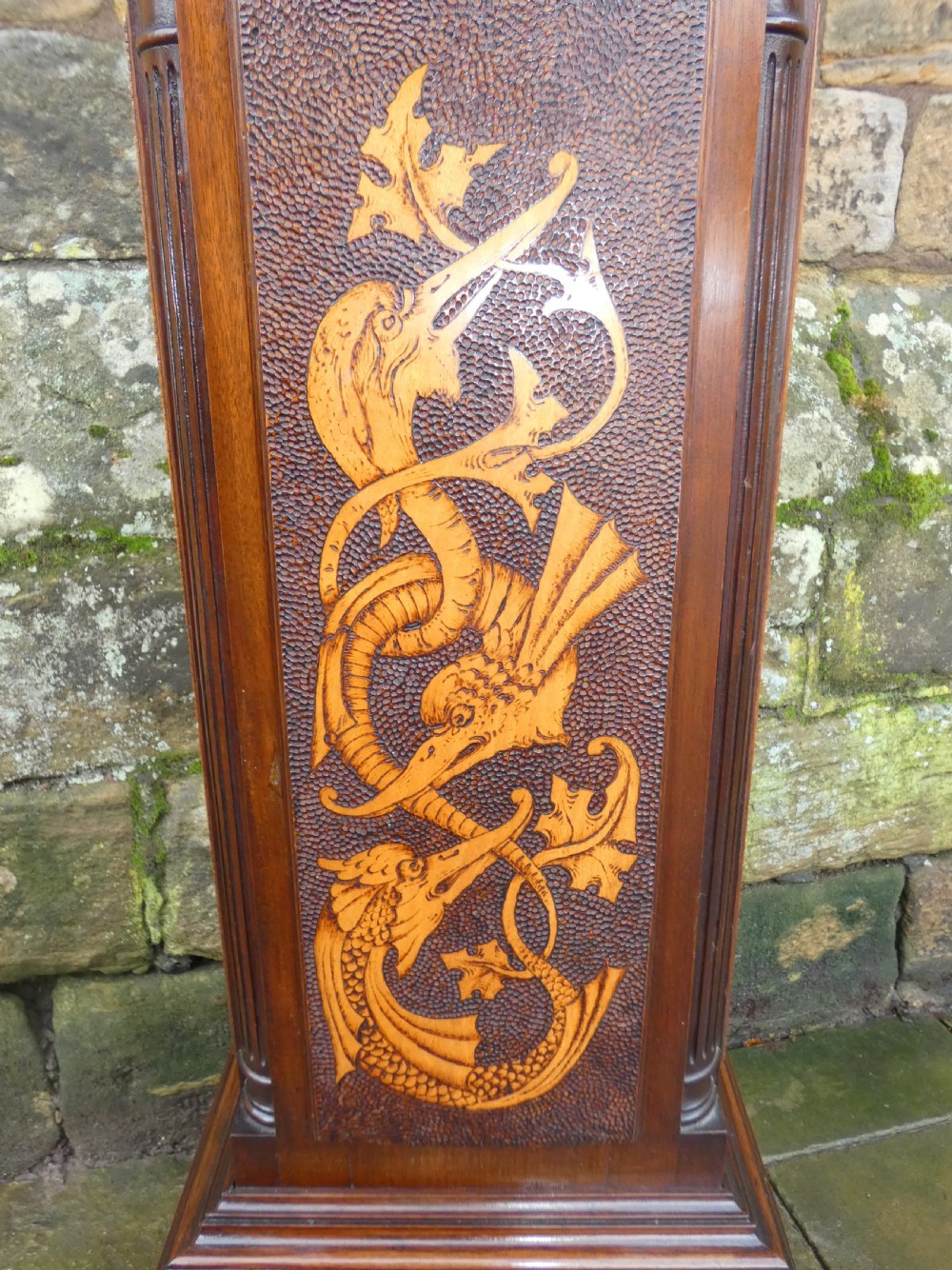 A square mahogany pedestal stand decorated with light-wood marquetry inlays featuring scrollwork and urn motifs on a stippled background. View III