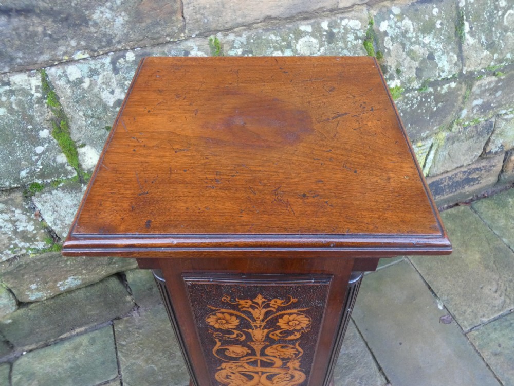 A square mahogany pedestal stand decorated with light-wood marquetry inlays featuring scrollwork and urn motifs on a stippled background. View V