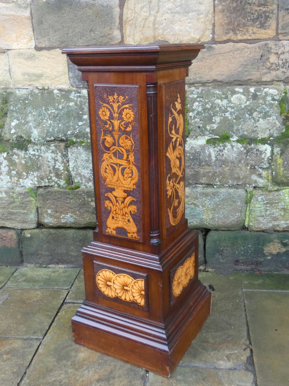 A square mahogany pedestal stand decorated with light-wood marquetry inlays featuring scrollwork and urn motifs on a stippled background. View VII