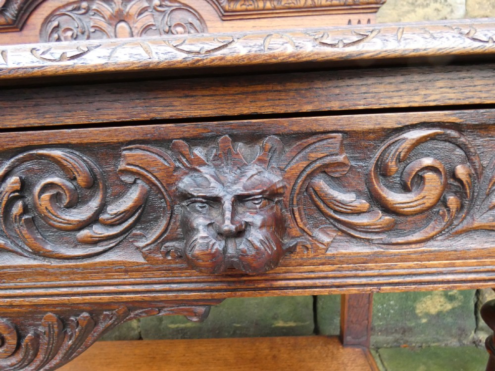 A dark carved oak hall table featuring a detailed relief gallery, two drawers with carved mask handles, turned legs, and a lower shelf. View II