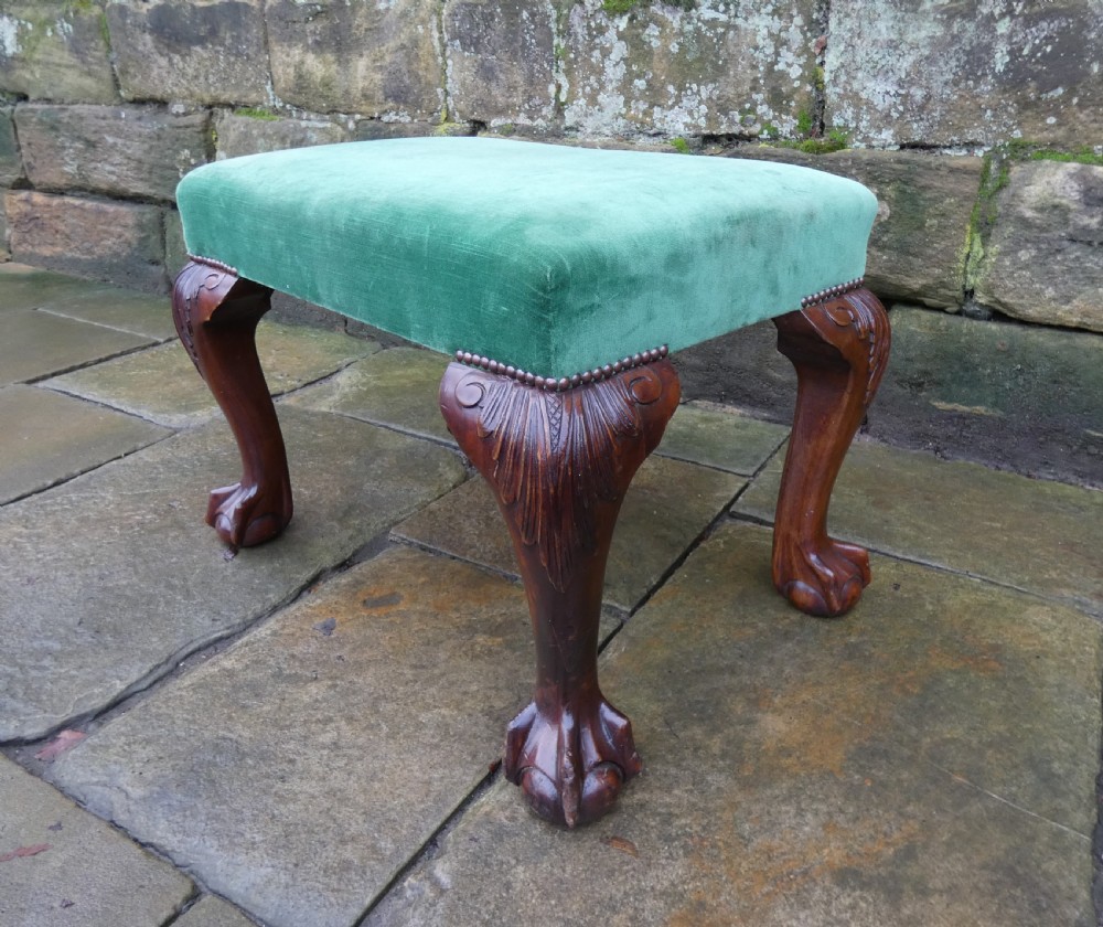 A low rectangular mahogany footstool with green velvet upholstery, studded border detail, and carved cabriole legs with claw and ball feet.