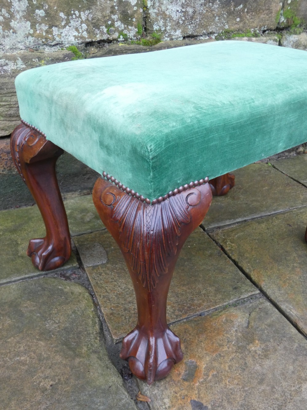 A low rectangular mahogany footstool with green velvet upholstery, studded border detail, and carved cabriole legs with claw and ball feet. View VI