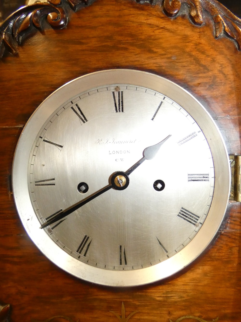 A William IV wooden bracket clock with carved foliate corner accents, brass scroll inlay, and a round dial displaying Roman numerals. View II