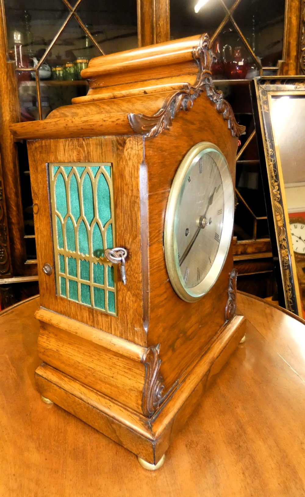 A William IV wooden bracket clock with carved foliate corner accents, brass scroll inlay, and a round dial displaying Roman numerals. View III